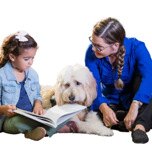 A woman and a girl sitting with a therapy dog in Calgary, engrossed in a book, showcasing the beauty of reading together.